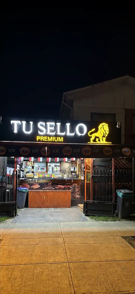 Fachada nocturna de Tú Sello Premium en Av. René Soriano 2121, con el letrero y el león iluminados